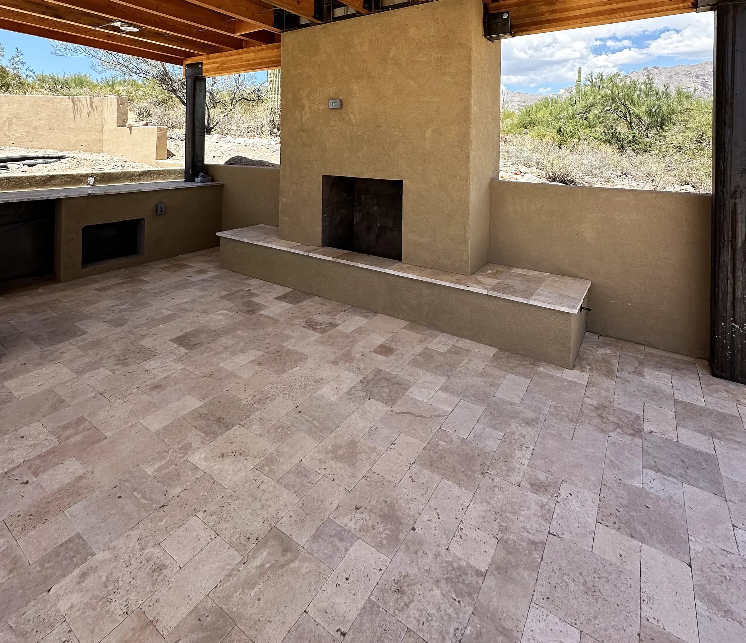 Finished stucco outdoor fireplace with a built-in seat bench on a travertine deck, looking out to the Sonoran desert