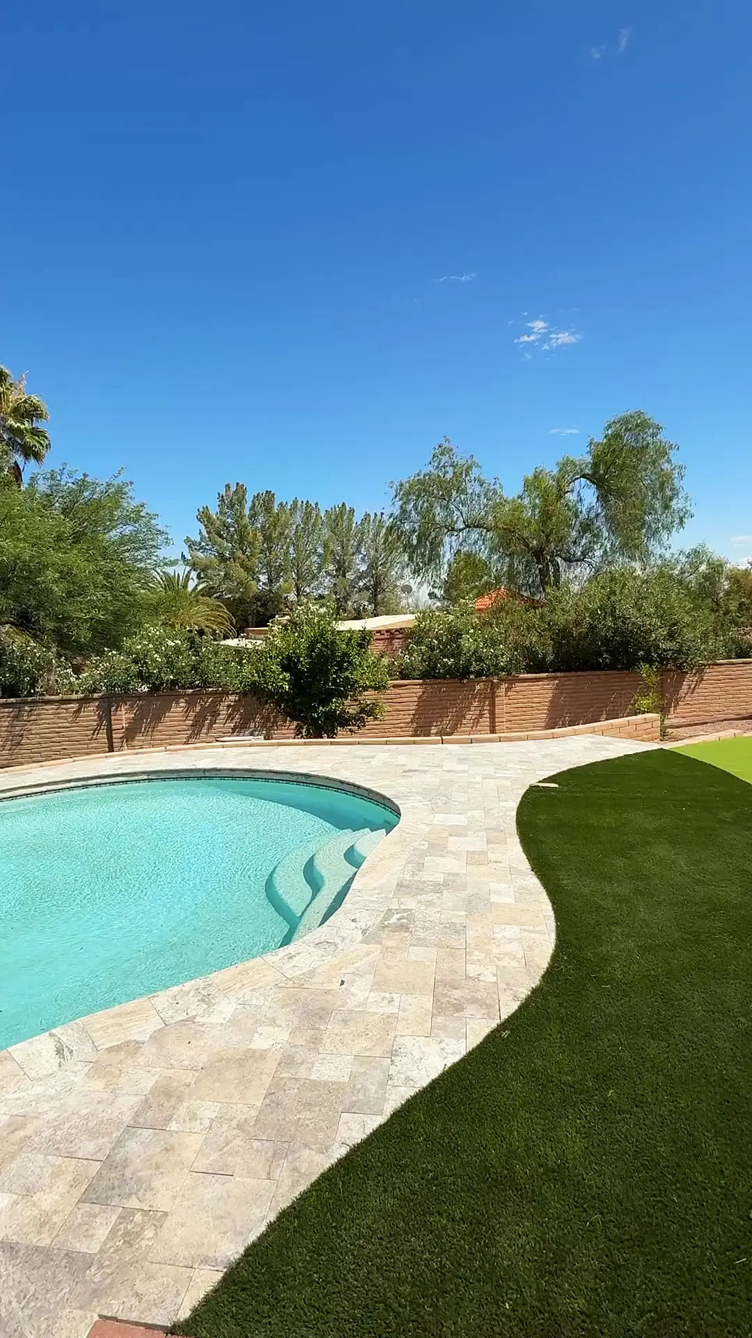 Silver travertine pool deck with coping curving into an artificial turf lawn in Tucson
