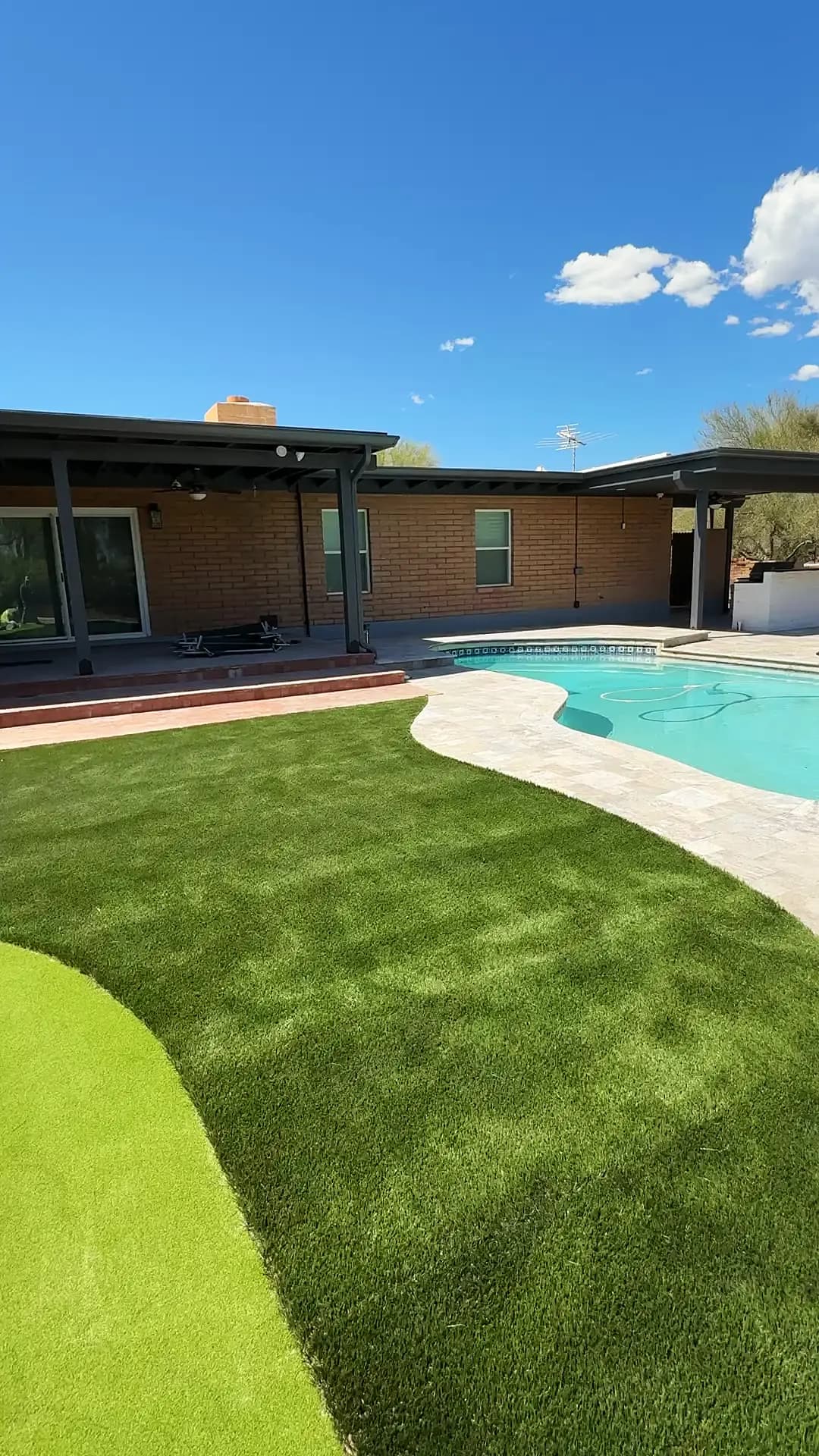 Artificial turf lawn sweeping past a pool toward a covered deck in Tucson